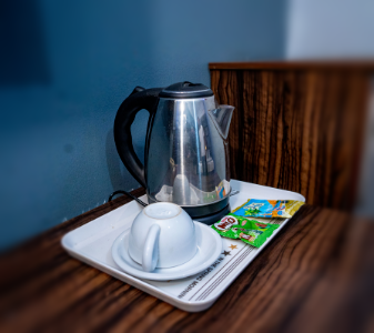 A hot water kettle, cup and milo and milk on the refreshment stand in the room